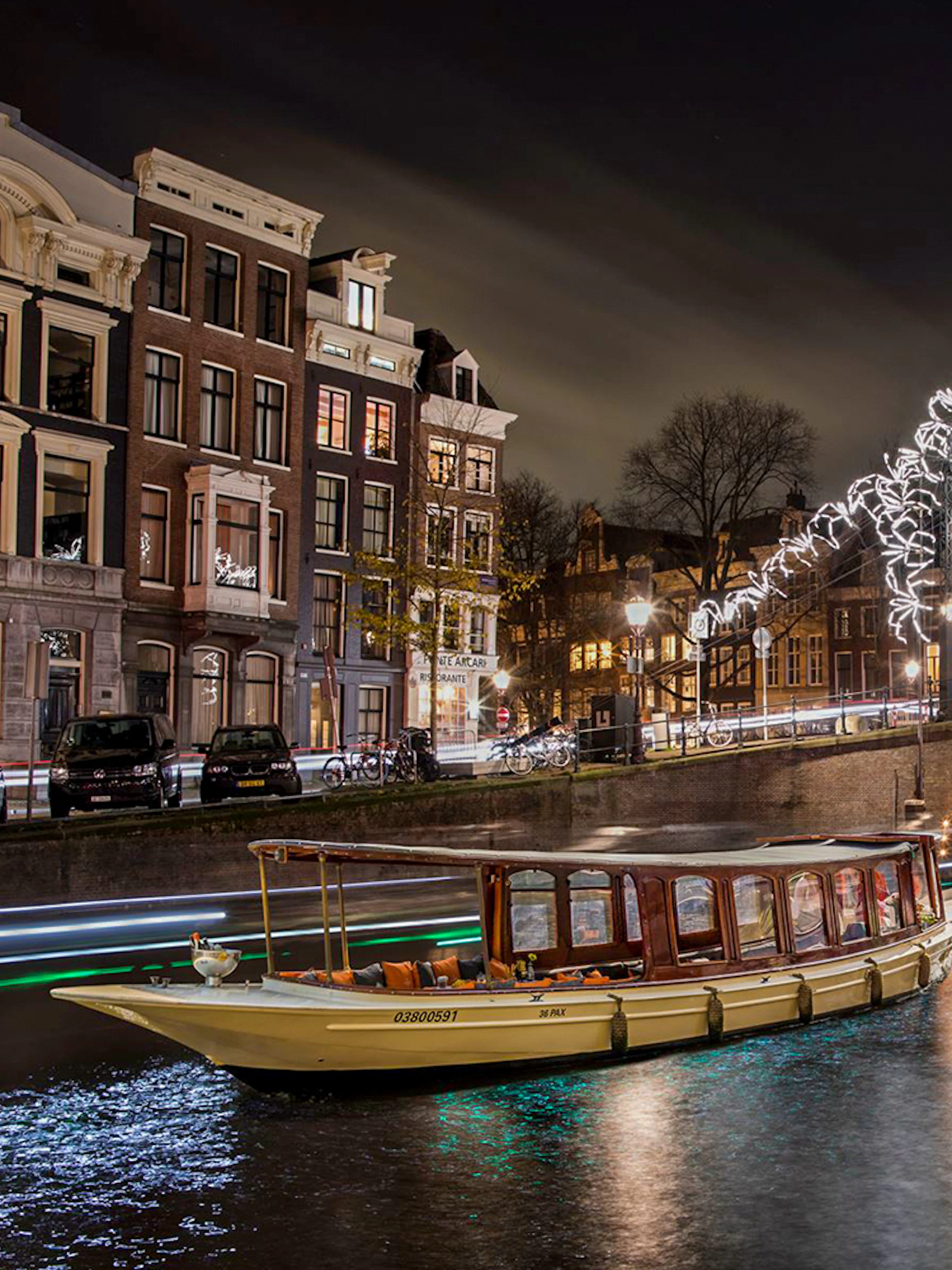 Canal boat cruising under illuminated bridge during Amsterdam Light Festival.