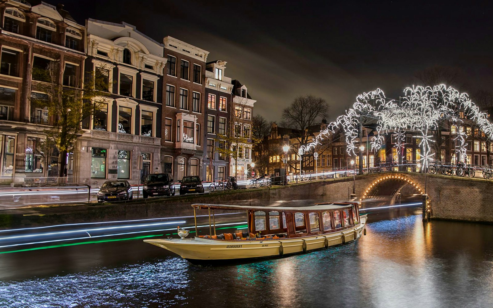 Canal boat cruising under illuminated bridge during Amsterdam Light Festival.