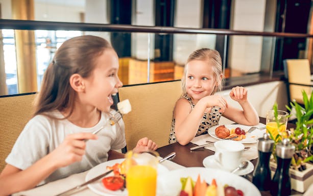 Children enjoying breakfast at Flora Danica with fruit and pastries on the table.