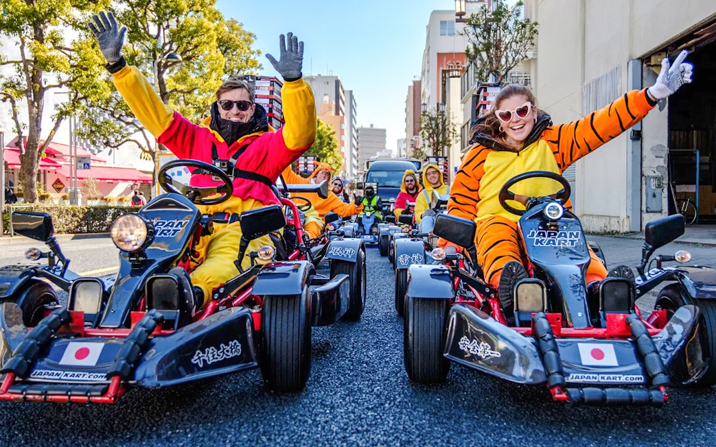 People in costumes driving go-karts on Asakusa streets during a tour.