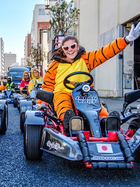 People in costumes driving go-karts on Asakusa streets during a tour.