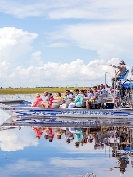 Airboat with tourists gliding through Everglades wetlands under a clear sky.