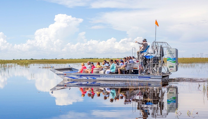Airboat with tourists gliding through Everglades wetlands under a clear sky.