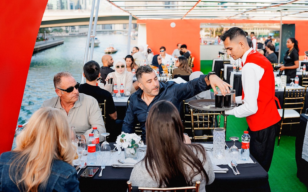 Guests dining on a sunset cruise in Dubai Marina with a waiter serving drinks.