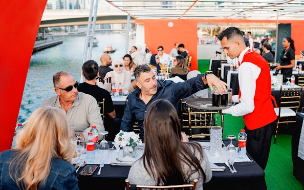 Guests dining on a sunset cruise in Dubai Marina with a waiter serving drinks.