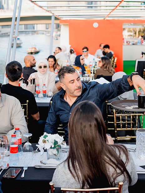 Guests dining on a sunset cruise in Dubai Marina with a waiter serving drinks.