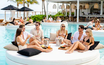 Group enjoying drinks on a floating island bed at FINNS Beach Party Lagoon Zone.