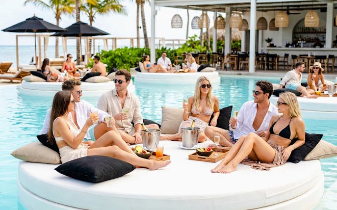 Group enjoying drinks on a floating island bed at FINNS Beach Party Lagoon Zone.