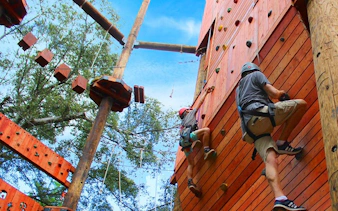 Climbers on a wooden wall at an 18-obstacle adventure course with a 50-foot freefall.