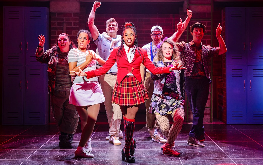 Cast performing on stage in Heathers: The Musical, vibrant costumes, energetic pose.
