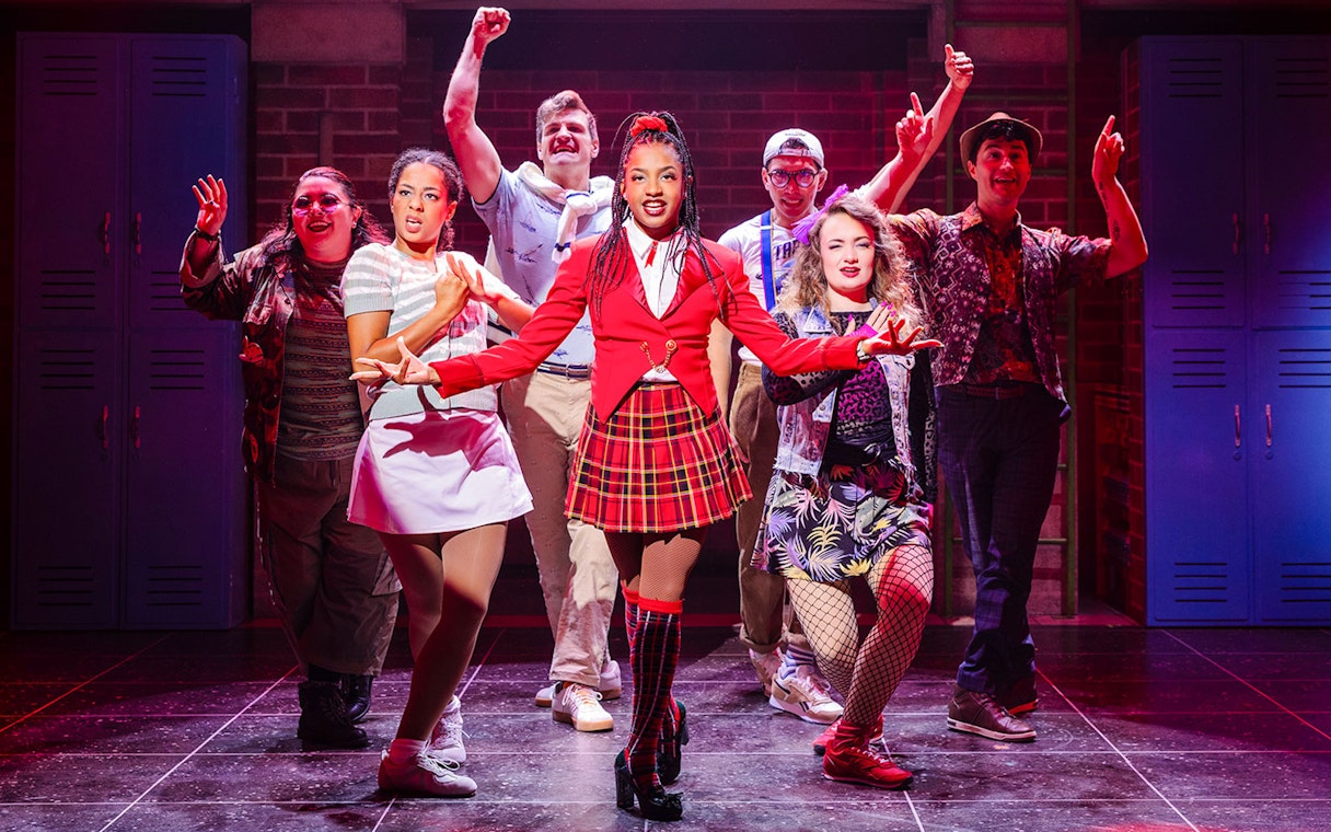 Cast performing on stage in Heathers: The Musical, vibrant costumes, energetic pose.