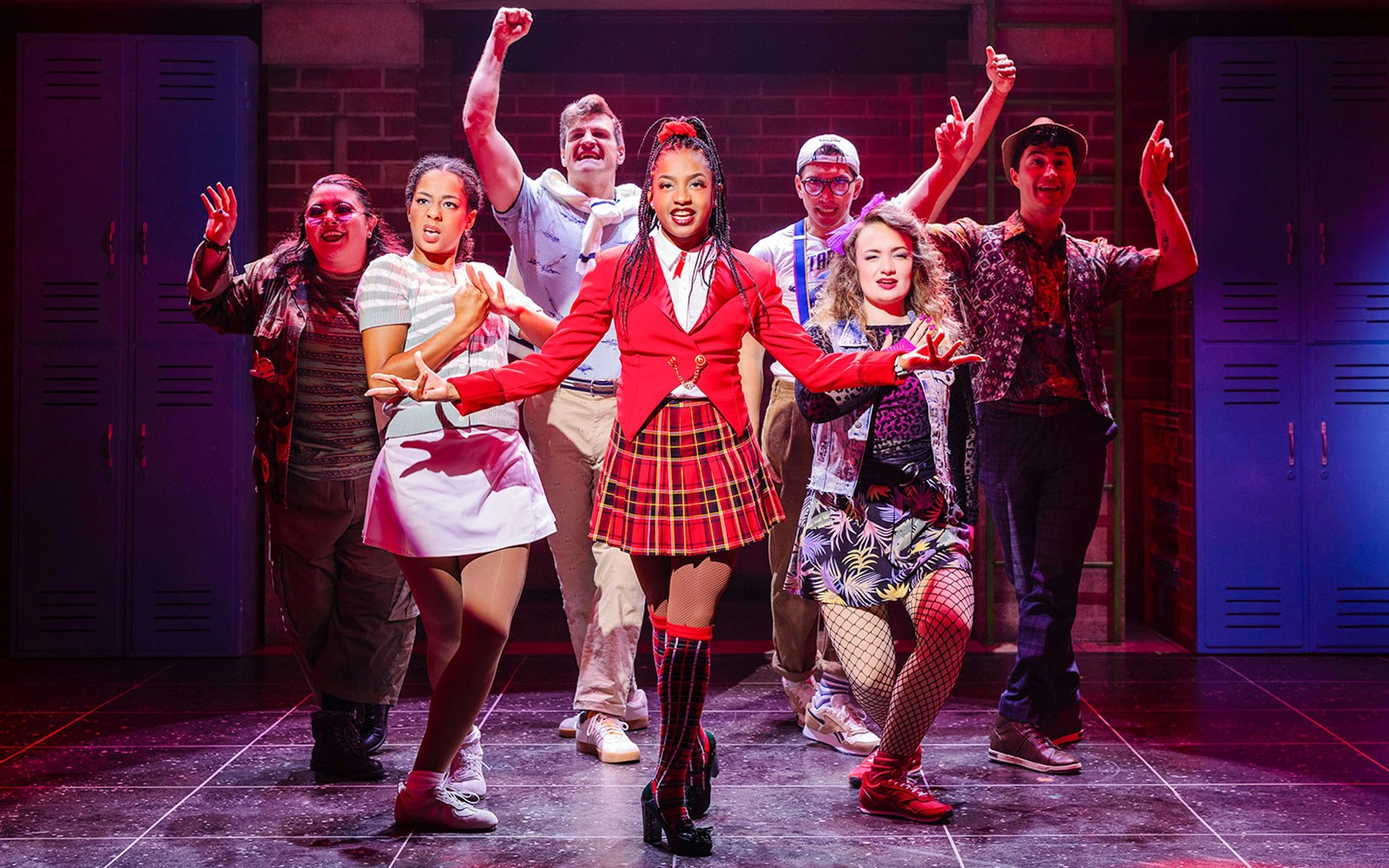 Cast performing on stage in Heathers: The Musical, vibrant costumes, energetic pose.
