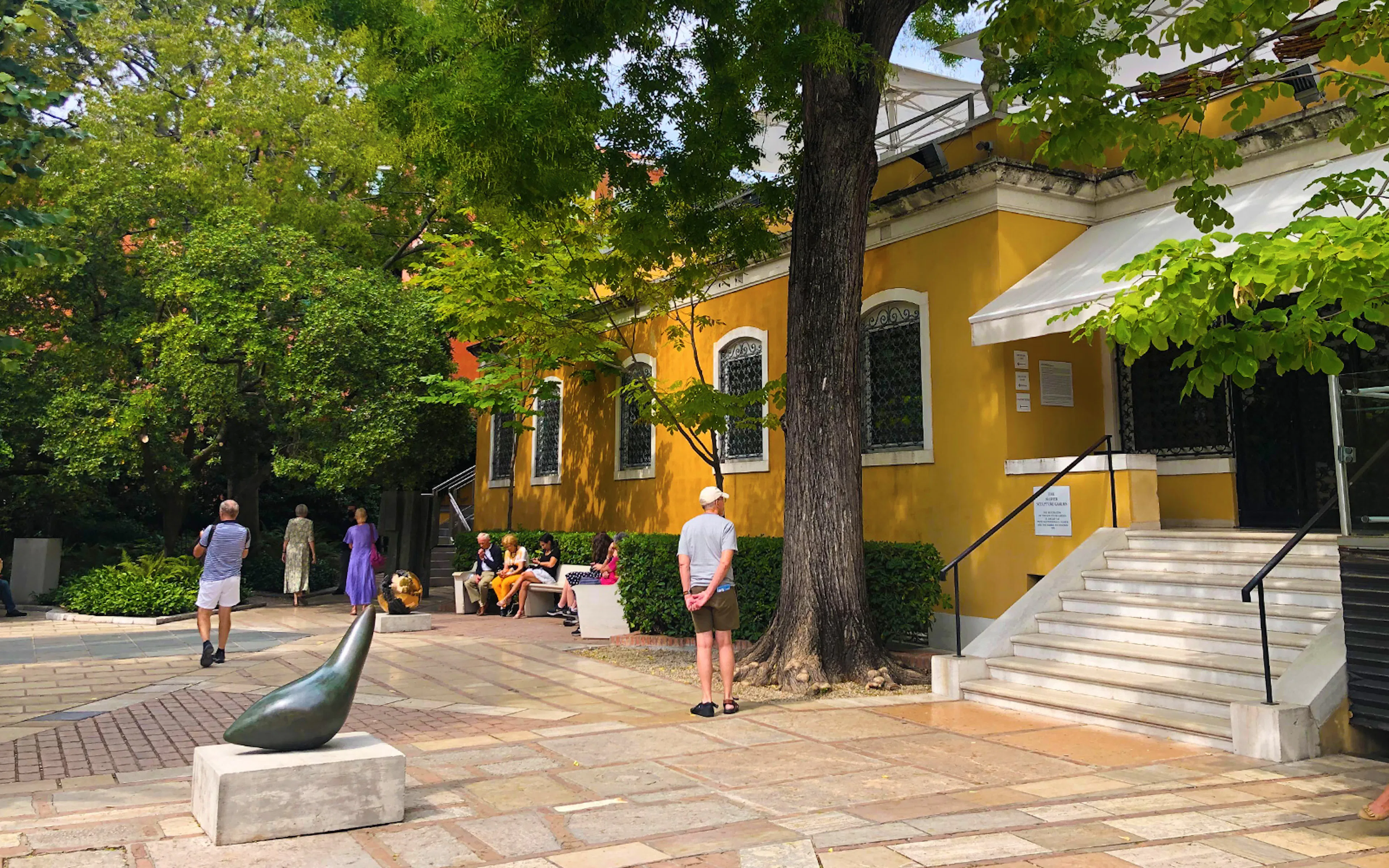Visitors outside the Peggy Guggenheim Collection in Venice, Italy, near a sculpture and yellow building.