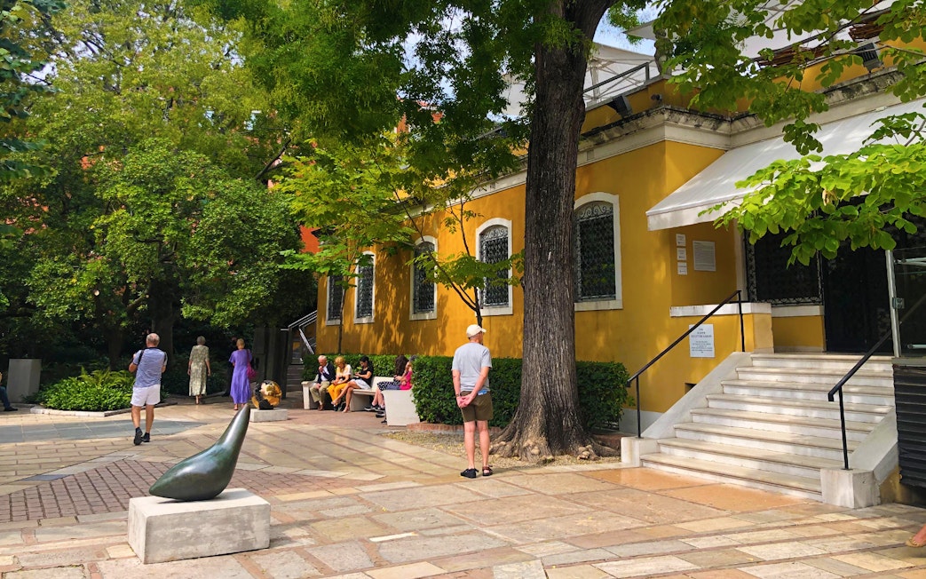 Visitors outside the Peggy Guggenheim Collection in Venice, Italy, near a sculpture and yellow building.