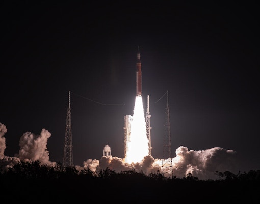 New Glenn rocket launching at Cape Canaveral, Florida, with fiery trail against a clear sky.