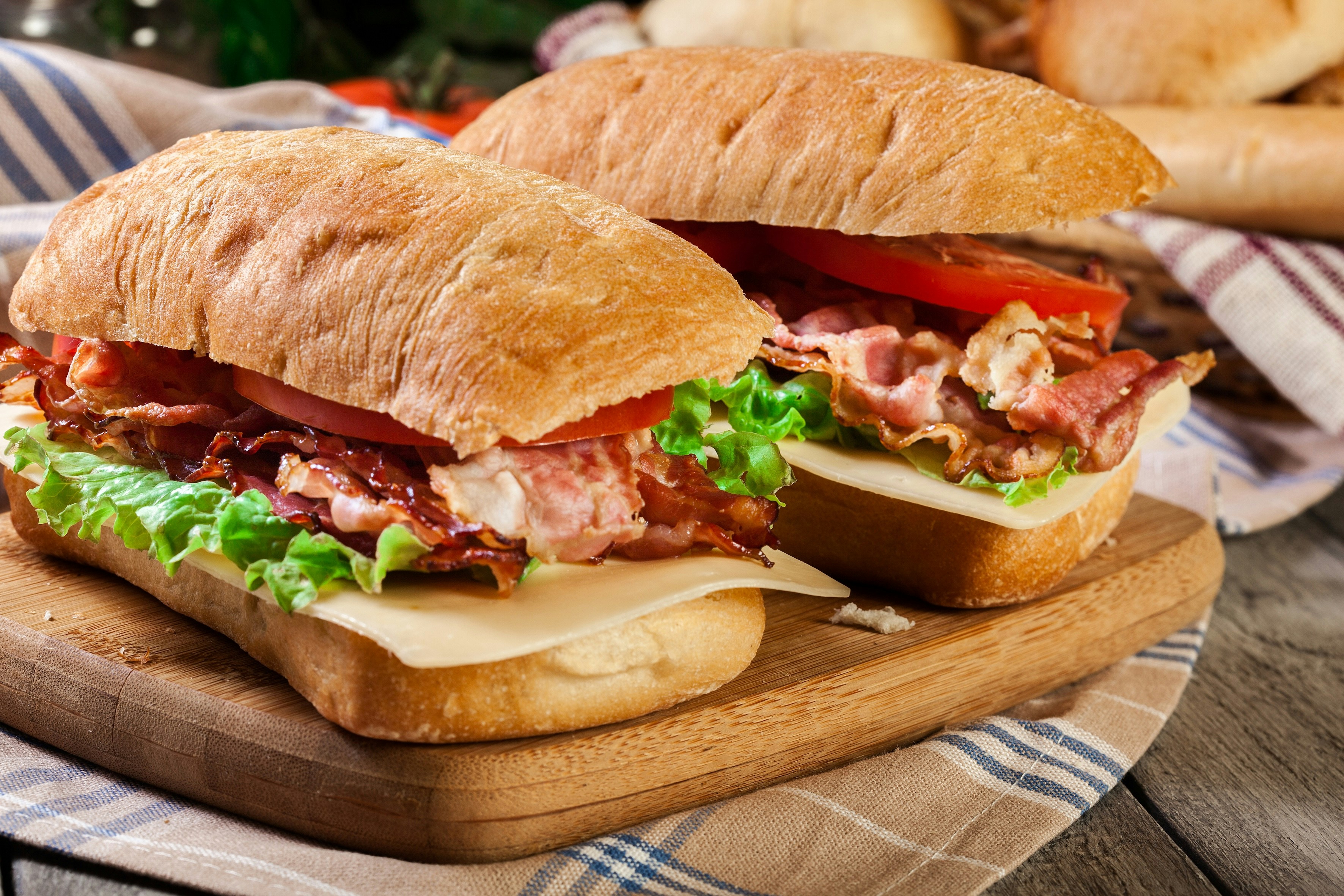 Panini sandwich with bacon, lettuce, tomato, and cheese on a wooden board.