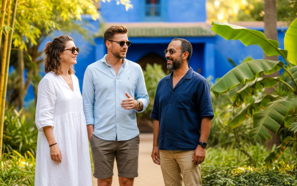 People with guide in Jardin Majorelle, Marrakech, surrounded by lush greenery and blue architecture.