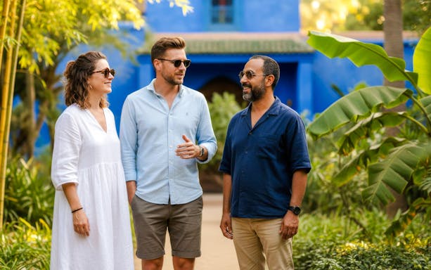 People with guide in Jardin Majorelle, Marrakech, surrounded by lush greenery and blue architecture.