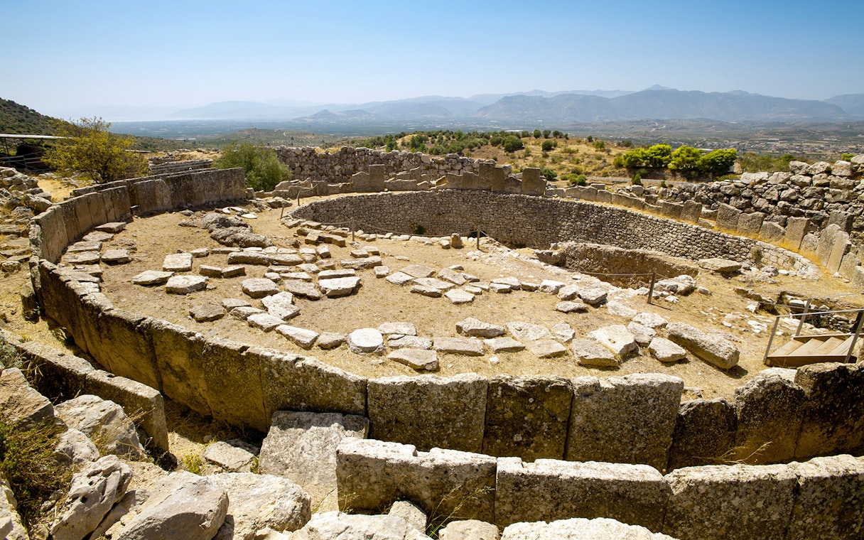 Mycenae archaeological site with ancient stone ruins and distant mountain view.