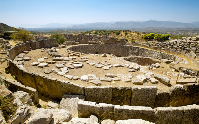 Mycenae archaeological site with ancient stone ruins and distant mountain view.