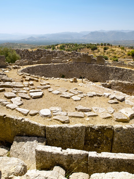 Mycenae archaeological site with ancient stone ruins and distant mountain view.