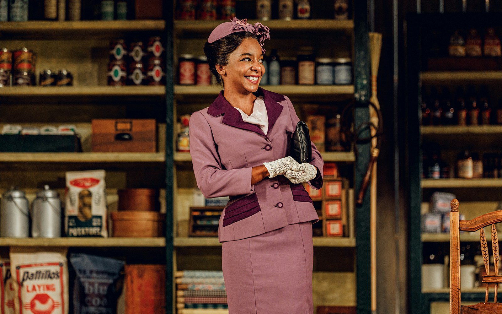 Woman in vintage attire smiling in front of a store shelf, related to "Purlie Victorious: A Non-Confederate Romp.