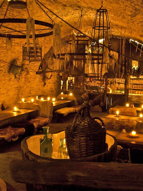 Medieval tavern interior with stone walls, wooden tables, and candlelight ambiance.