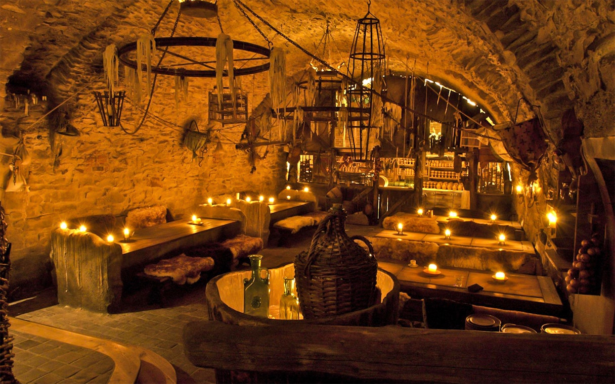 Medieval tavern interior with stone walls, wooden tables, and candlelight ambiance.