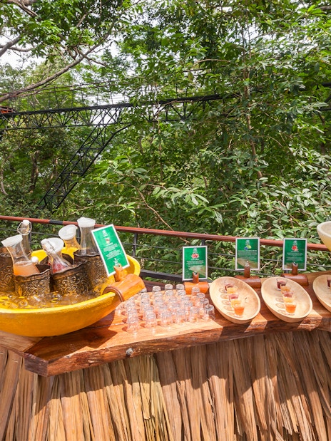 Juices and water on a wooden table at Hanuman World, surrounded by lush greenery.