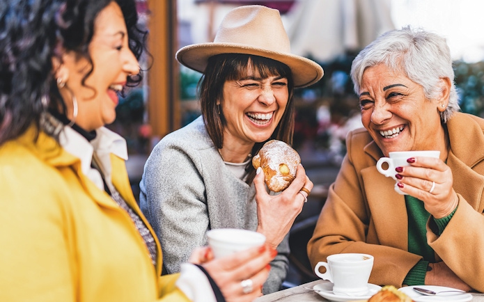 Senior women laughing at a bar, enjoying coffee and pastries.