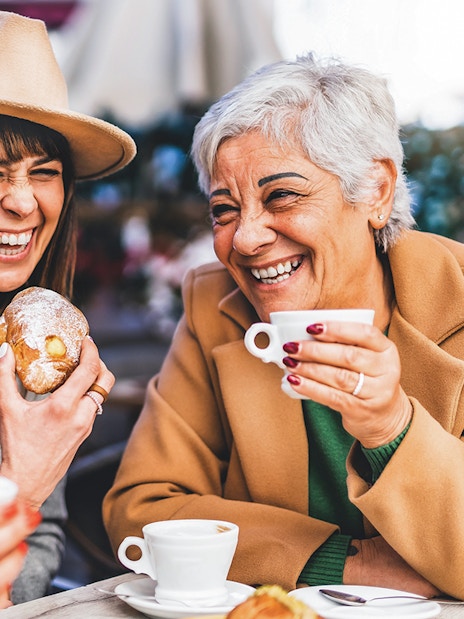 Senior women laughing at a bar, enjoying coffee and pastries.