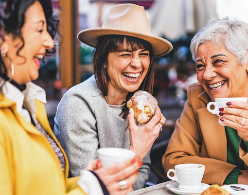 Senior women laughing at a bar, enjoying coffee and pastries.