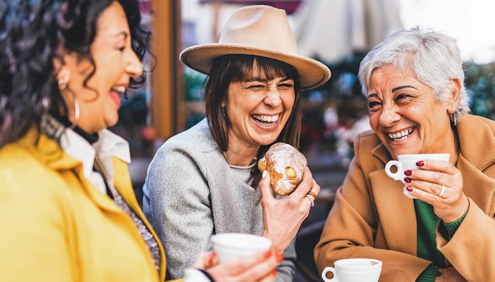 Senior women laughing at a bar, enjoying coffee and pastries.