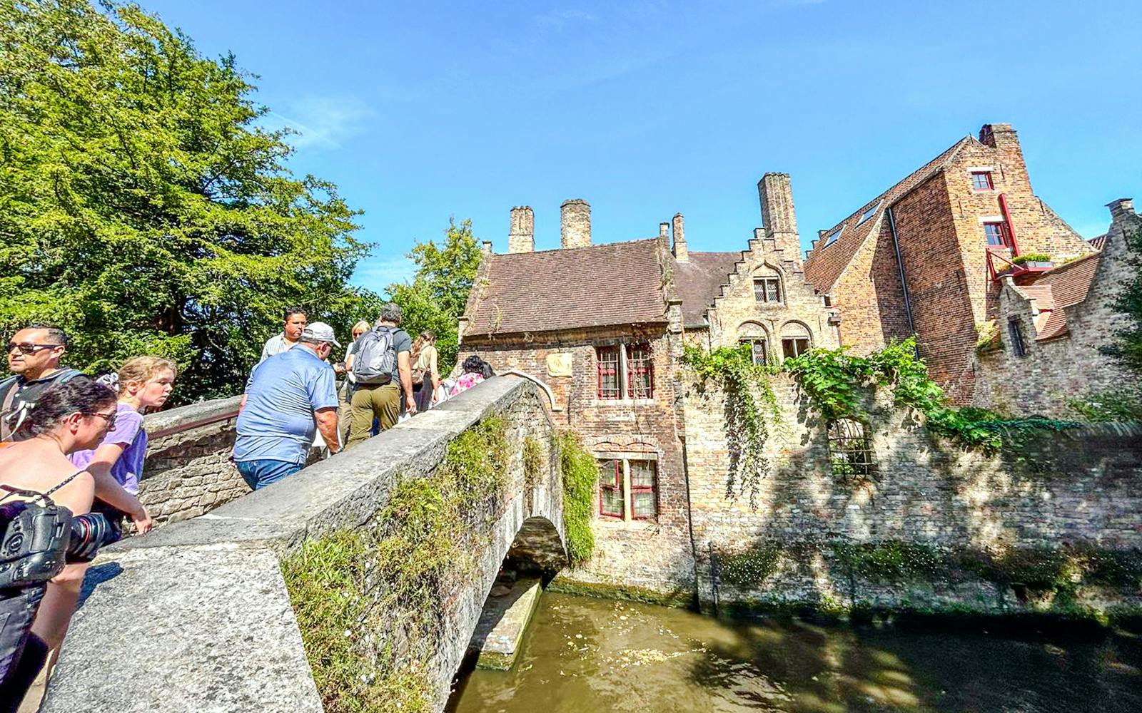Tourists crossing Bonifacius Bridge in Bruges, Belgium, with historic buildings in the background.