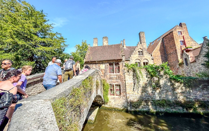 Tourists crossing Bonifacius Bridge in Bruges, Belgium, with historic buildings in the background.