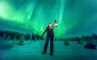 Person holding lantern under northern lights during group tour.