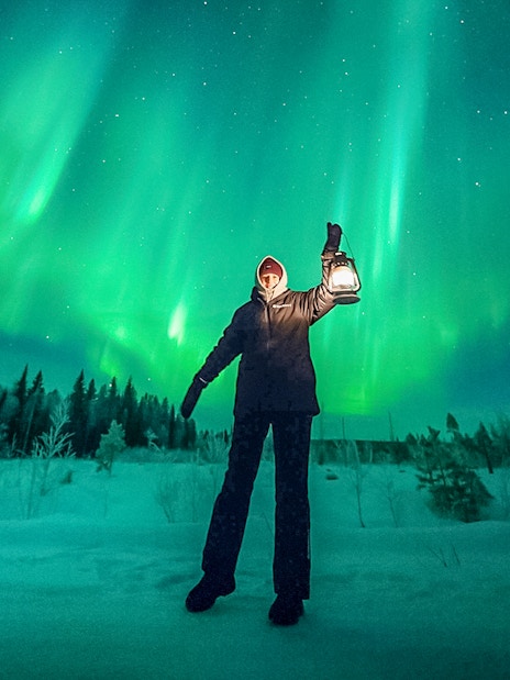 Person holding lantern under northern lights during group tour.