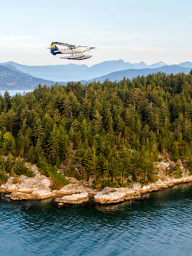 Seaplane flying over forested coastline near Vancouver.
