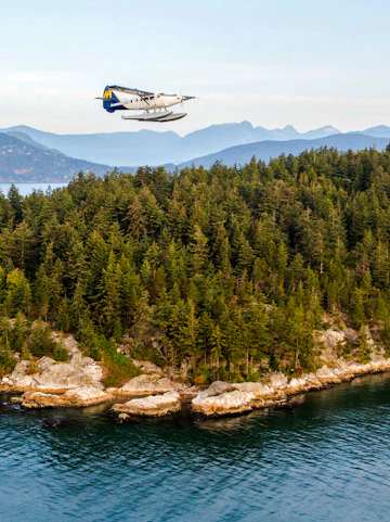 Seaplane flying over forested coastline near Vancouver.