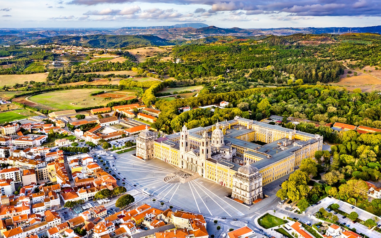 Aerial view of the National Palace of Mafra, Portugal, surrounded by lush greenery and town buildings.