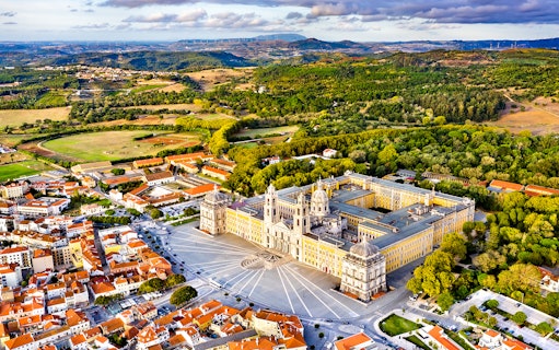 Aerial view of the National Palace of Mafra, Portugal, surrounded by lush greenery and town buildings.
