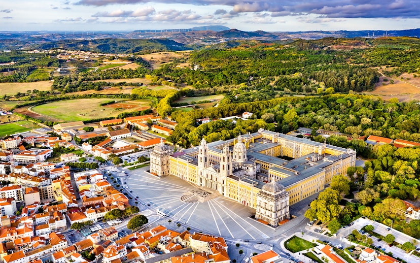 Aerial view of the National Palace of Mafra, Portugal, surrounded by lush greenery and town buildings.