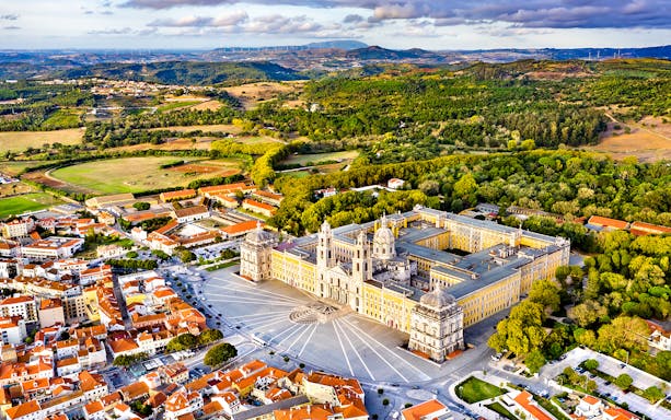 Aerial view of the National Palace of Mafra, Portugal, surrounded by lush greenery and town buildings.