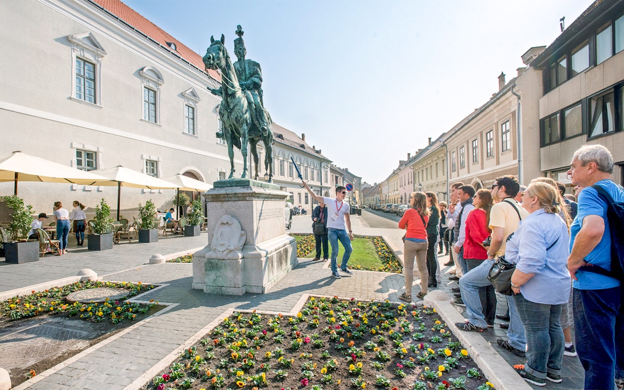 Tour group with guide at equestrian statue in Budapest.