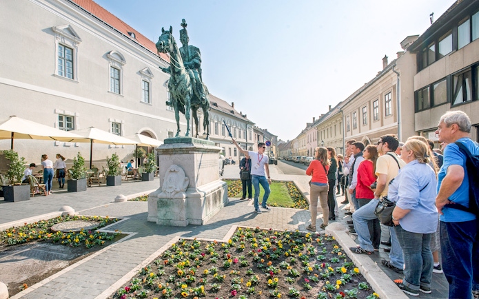 Tour group with guide at equestrian statue in Budapest.