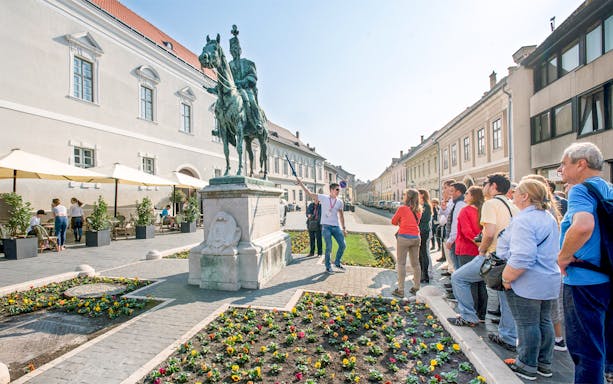 Tour group with guide at equestrian statue in Budapest.
