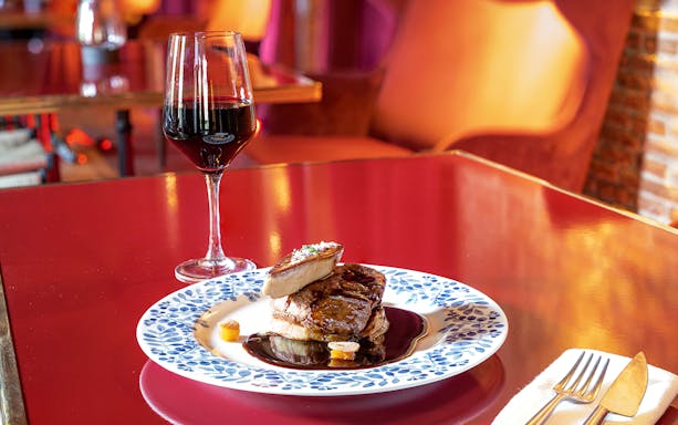 Steak with foie gras and red wine on a red table, part of a gastronomic experience.