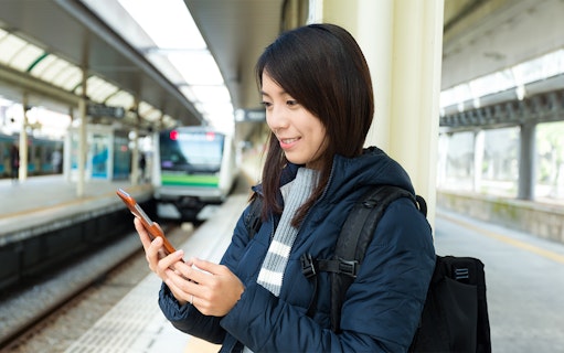 Person using phone at a train station platform in Japan, Suica IC Card context.