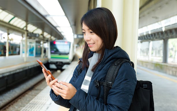 Person using phone at a train station platform in Japan, Suica IC Card context.