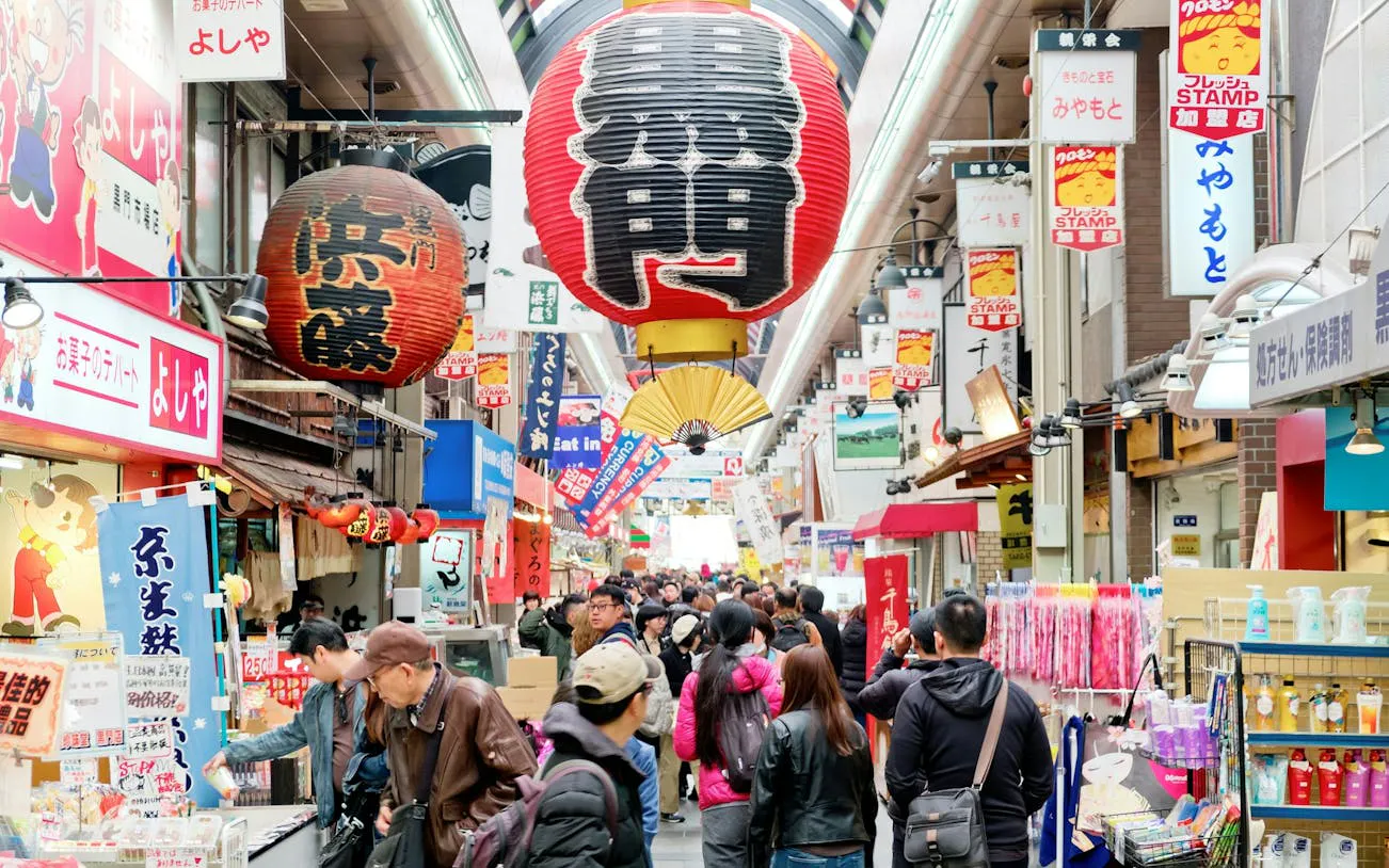 Crowded Kuromon Ichiba Market in Osaka with vibrant signs and lanterns.